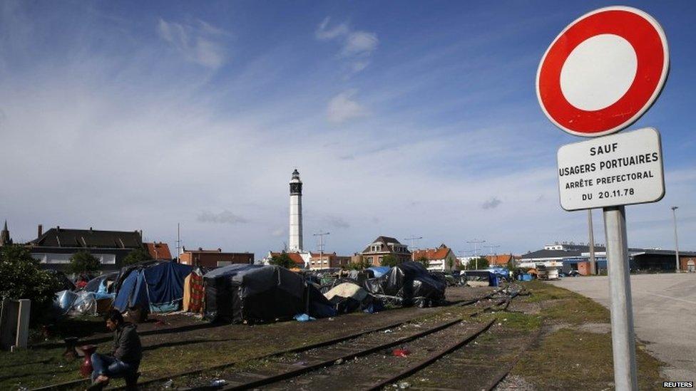 An Afghan migrant sits at the entry of a tent camp of makeshift shelters on the harbour in Calais