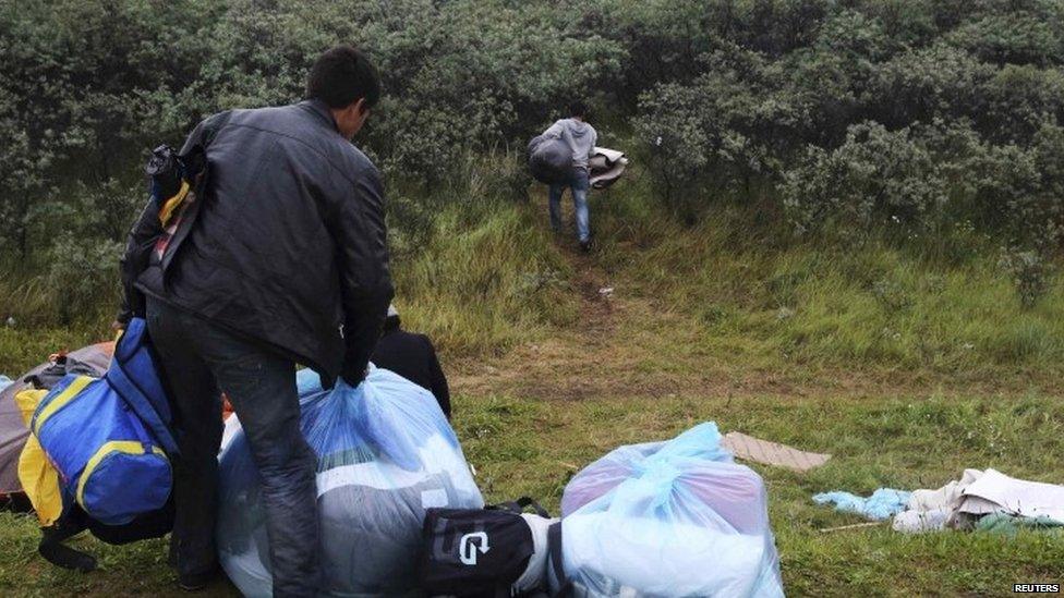 An Afghan migrant carries his belongings protected in plastic bags as he flees his makeshift shelter at the harbour in Calais