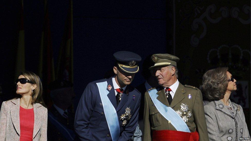 Spain's Crown Prince Felipe (2nd L) and King Juan Carlos talk as Princess Letizia (L) and Queen Sofia (R) watch a military parade during Spain's National Day in Madrid