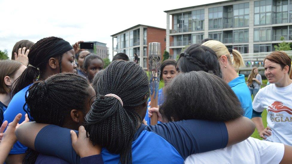 A group of girls gather around the Queen's Relay Baton