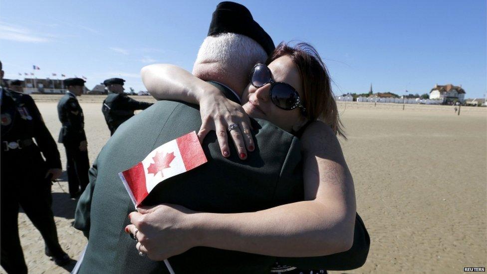 A woman holding a Canadian flag hugs a man