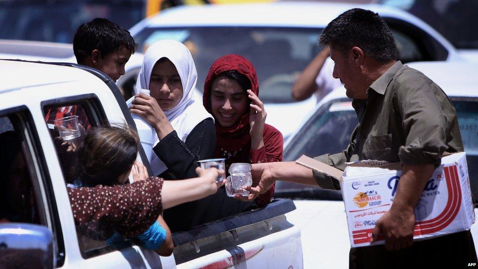 Iraqi families are given water as they gather at a checkpoint near Erbil, the autonomous Kurdistan region, on 10 June 2014.