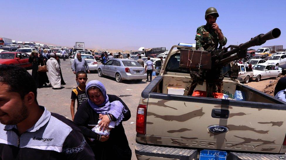 Iraqi families fleeing violence in the northern Nineveh province gather at a checkpoint about 40km west of Erbil, on 10 June 2014