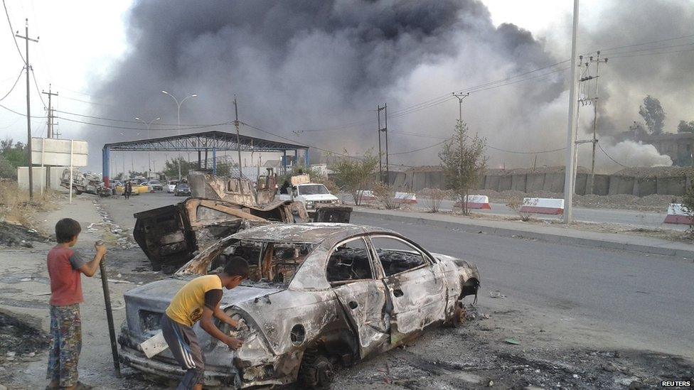 Civilian children stand next to a burnt vehicle during clashes between Iraqi security forces and al Qaeda-linked Islamic State in Iraq and the Levant (ISIS) in the northern Iraq city of Mosul, 10 June 2014