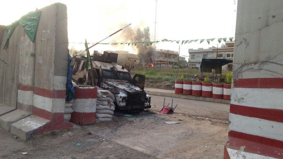 A burned out vehicle is seen with a fire burning behind it in the Iraqi city of Mosul