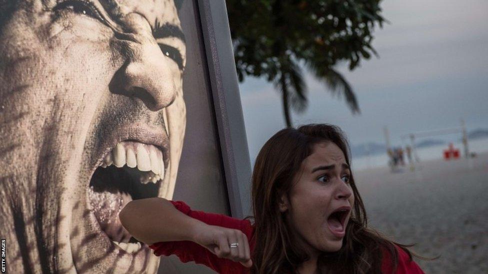 A tourist jokes in front of an advertisement featuring the portrait of Uruguay's forward Luis Suarez at Copacabana beach in Rio de Janeiro