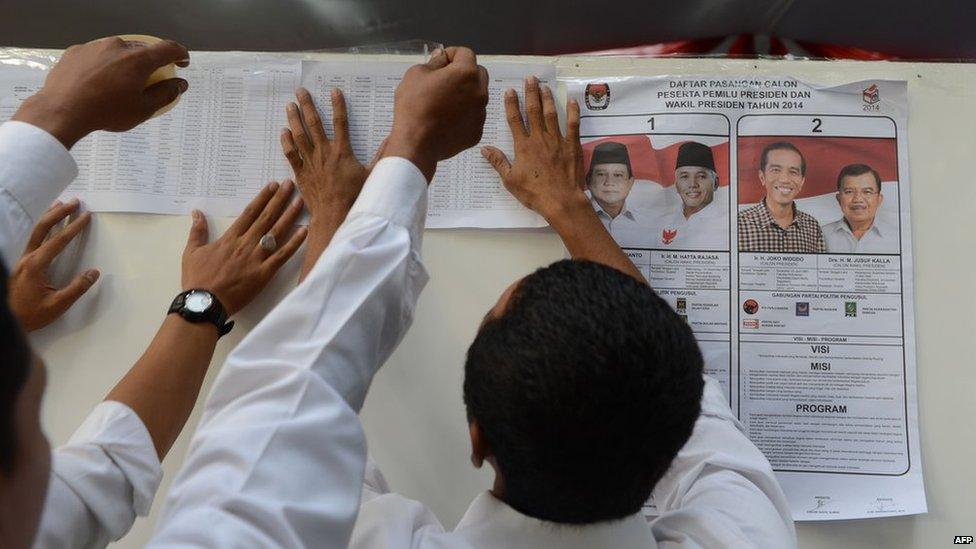 Poll workers post voters list at a polling centre in Jakarta next to a poster showing the two presidential candidates Prabowo Subianto (L) with running mate Hatta Rajasa and Joko Widodo with running mate Jusuf Kalla (R) as voting opens in Jakarta on 9 July, 2014