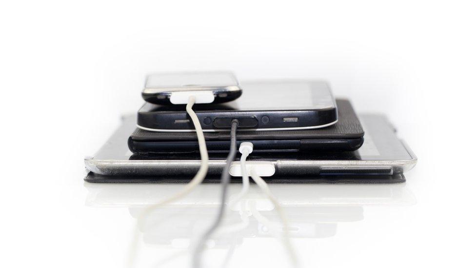 A stack of electronic items with charger wires attached