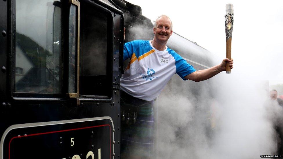 David Sedgwick holds baton from cab of vintage train as steam billows around him