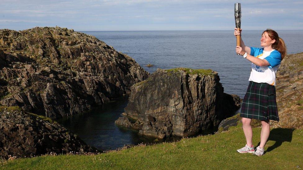 Kilted baton bearer poses at the edge of some sea cliffs