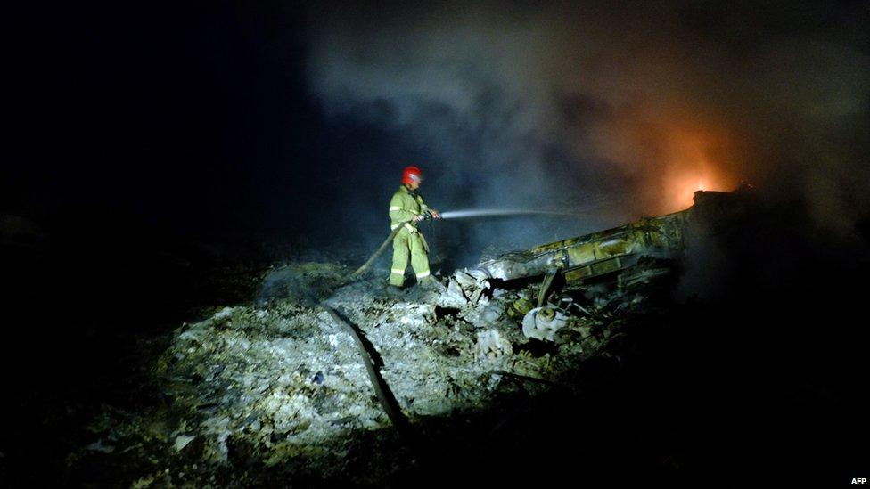 A firefighter sprays water to extinguish a fire, on 17 July 2014, from the wreckage of the crashed Malaysian airliner