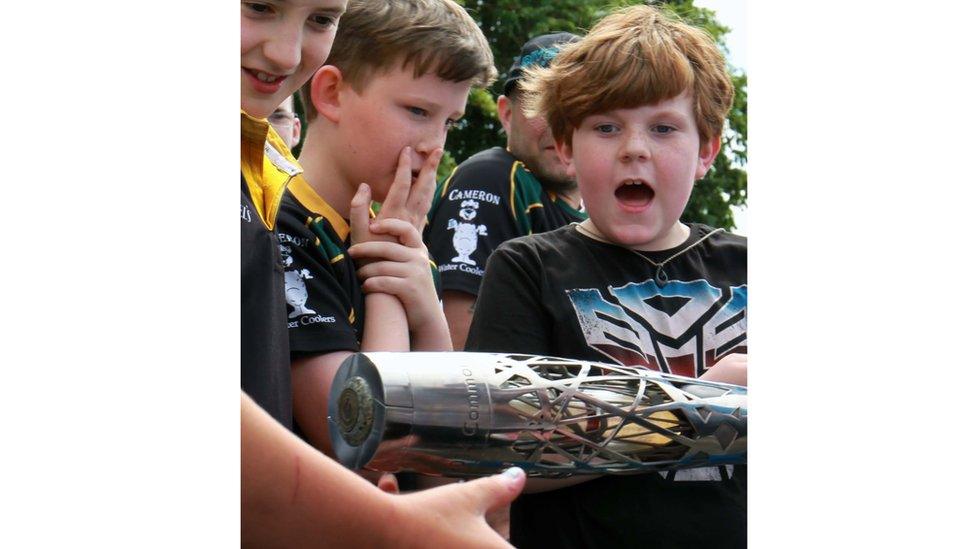 Open-mouthed schoolboy holds baton as his friends admire it