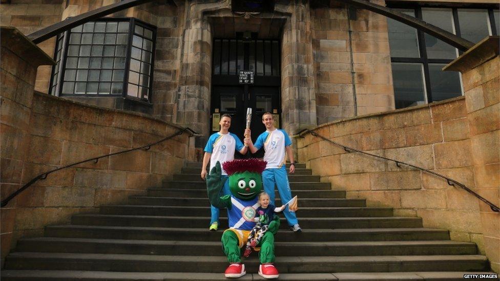 Batonbearer 025 William Mitchell and Batonbearer 026 Michael Aldridge, with Clyde the Glasgow 2014 mascot, hold the Glasgow 2014 Queen"s Baton at the Glasgow School of Art