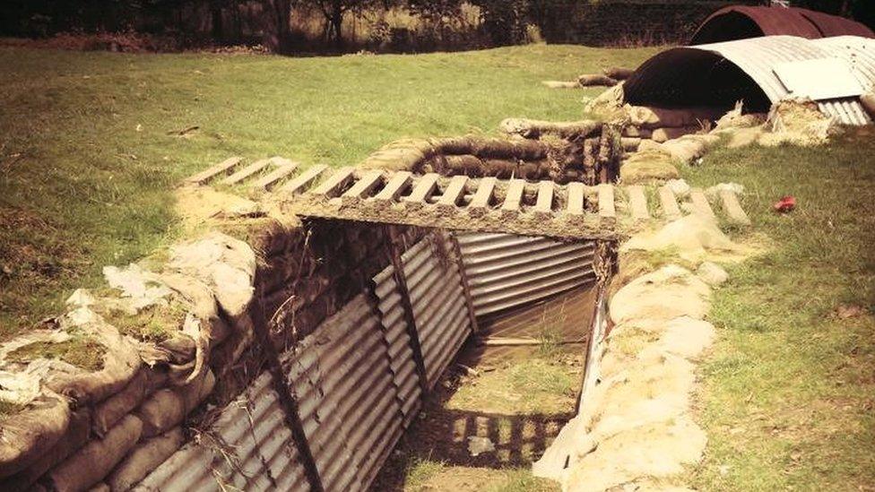 A trench with corrugated metal walls and a wooden ladder over the top to allow people to get from one side to the other