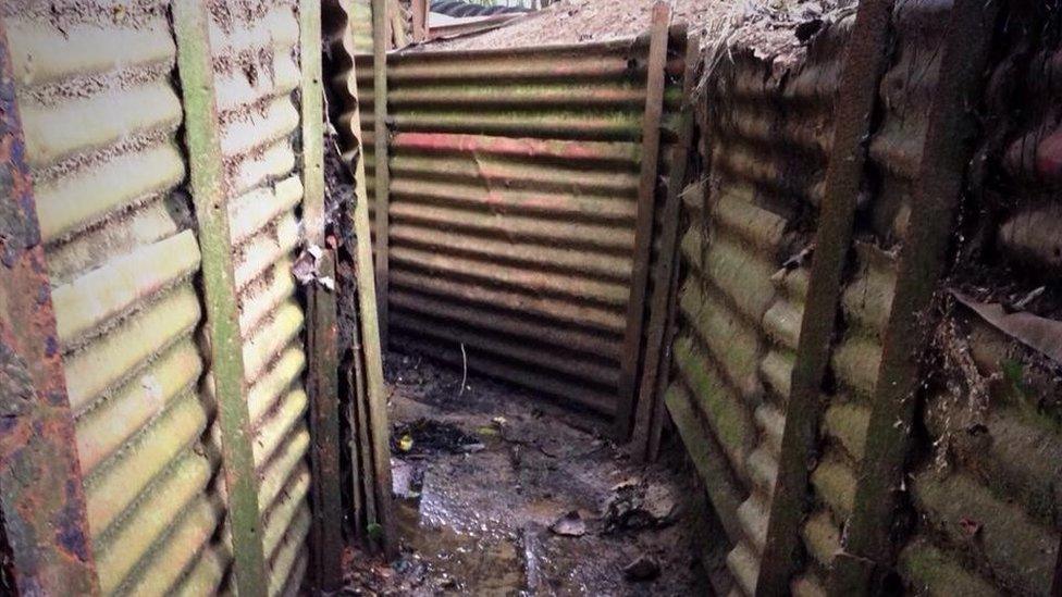 A corrugated metal trench with a muddy floor