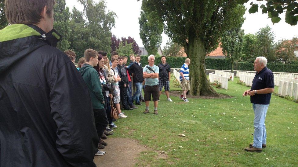 A tour guide addresses a group of people in a cemetery