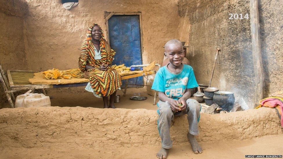 Haja sitting on a bed in her house looking at her grandson in a camp in Darfur, Sudan - 2014