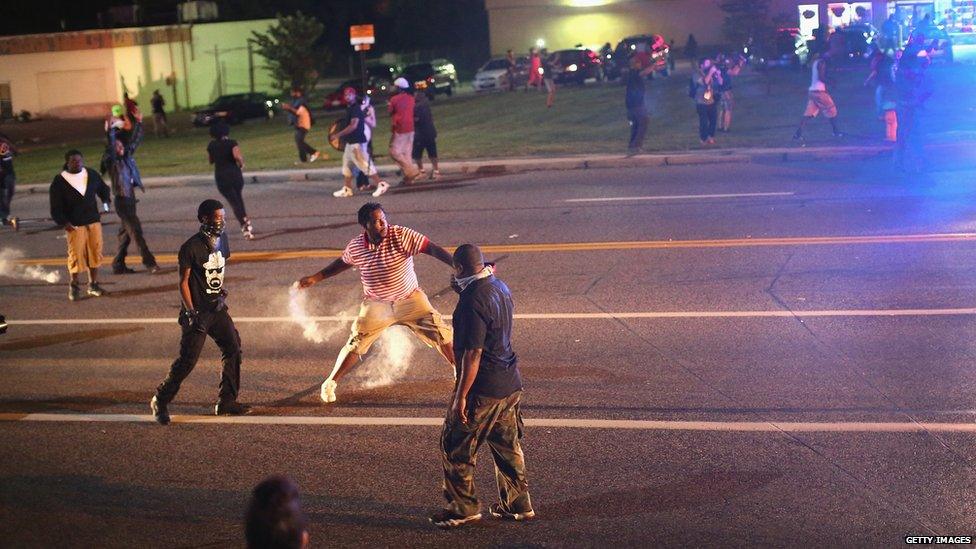 A demonstrator protesting the killing of teenager Michael Brown by a Ferguson police officer throws a tear gas grenade back toward police after the protest was attacked by police in Ferguson, Missouri, 17 August 2014