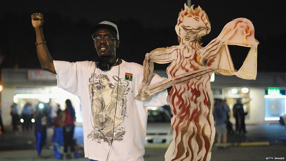 A protester holds up a board showing a flaming scales of justice in Missouri