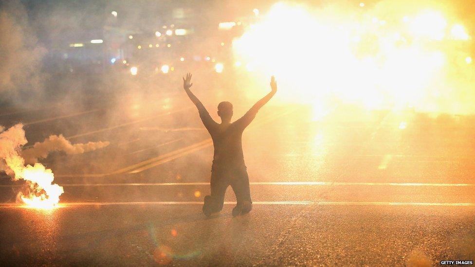 Tear gas envelops a woman kneeling in the street with her hands in the air after a demonstration over the killing of teenager Michael Brown by a Ferguson police officer in Ferguson, Missouri, 17 August 2014