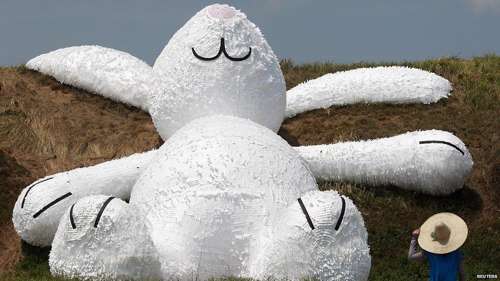 A person stands in front of a 25.3-meter-long giant rabbit designed by Dutch artist Florentijn Hofman in an old aircraft hangar as part of the Taoyuan Land Art Festival in Taoyuan, northern Taiwan, on 3 September, 2014