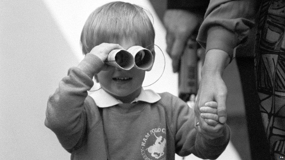 Prince Harry, three-year-old son of the Prince and Princess of Wales, zooms in on the army of press photographers waiting outside his new kindergarten in London's Notting Hill, using a homemade pair of binoculars.