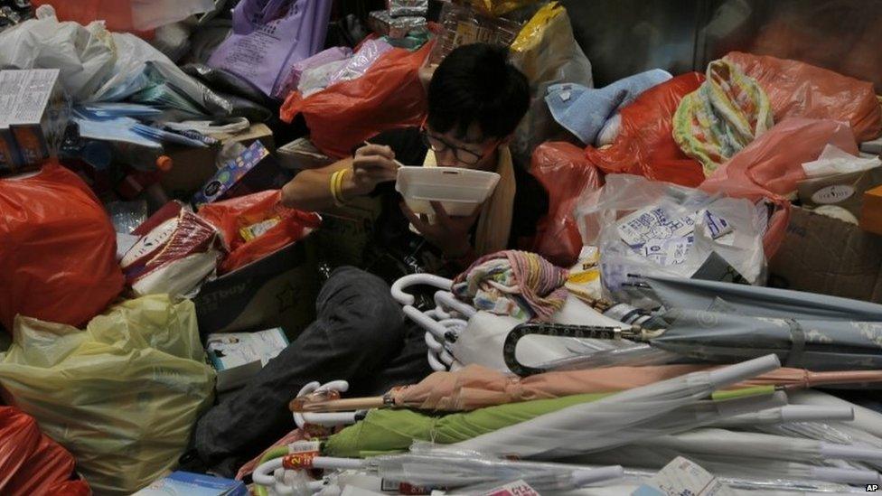 A pro-democracy protester eats takeout food by a stack of umbrellas which pro-democracy activists have been using to shield themselves from pepper spray in Hong Kong on 29 September 29 2014.