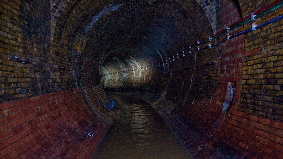 Heavy rusty rings line the tunnel walls beside the Fleet