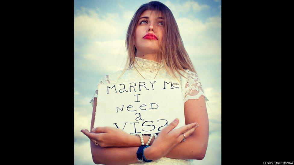 Women holding a sign saying 'marry me I need a visa'