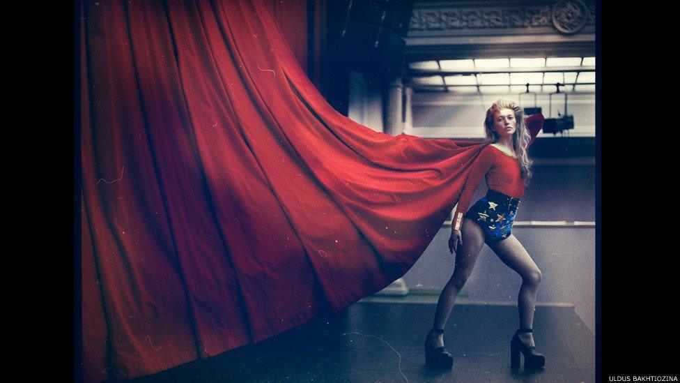 Woman in gymnastic outfit holding up a red curtain