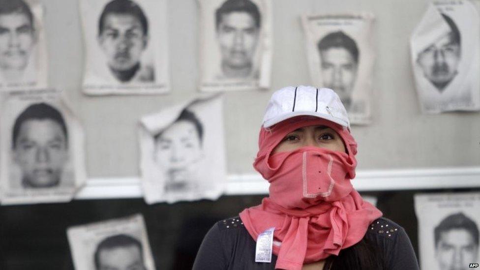 A hooded student is seen in front of the portraits of some of the 43 missing students at the tollbooths on the Chilpancingo-Acapulco highway on 12 November, 2014.