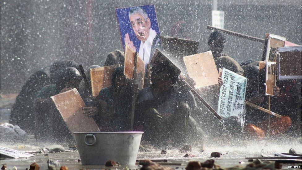 Supporters of Satguru Rampalji Maharaj, a self-styled "godman" take shelter under placards as they are hit by a police water cannon during a protest outside the ashram of Rampal in Hisar in the northern Indian state of Haryana November 18, 2014.