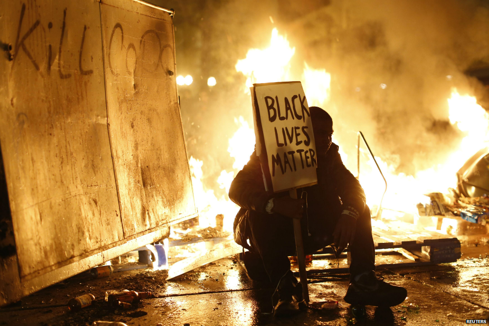 A protester sits in front of a street fire during a demonstration over the Michael Brown decision in Oakland, California - 25 November 2014