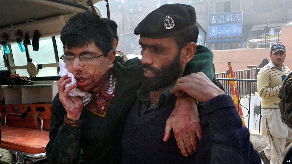 A security guard helps a student after a gun attack at a school in Peshawar