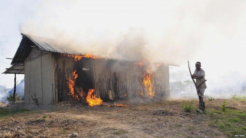 A tribal plantation worker holds a bow and arrow as he stands next to a burning house belonging to indigenous Bodo tribesmen after ethnic clashes in Balijuri village, in Sonitpur district in the northeastern Indian state of Assam December 24, 2014.