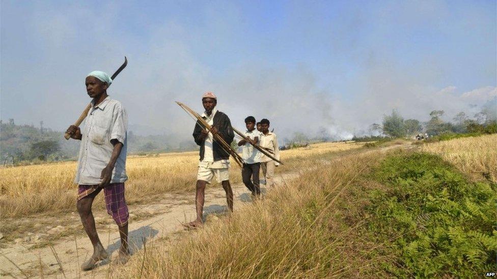 Indian villagers carrying bows and arrows walk away from the homes of members of the Bodo community as they burn in the village of Tenganala in Sonitpur District, some 250kms east of Guwahati on December 24, 2014.