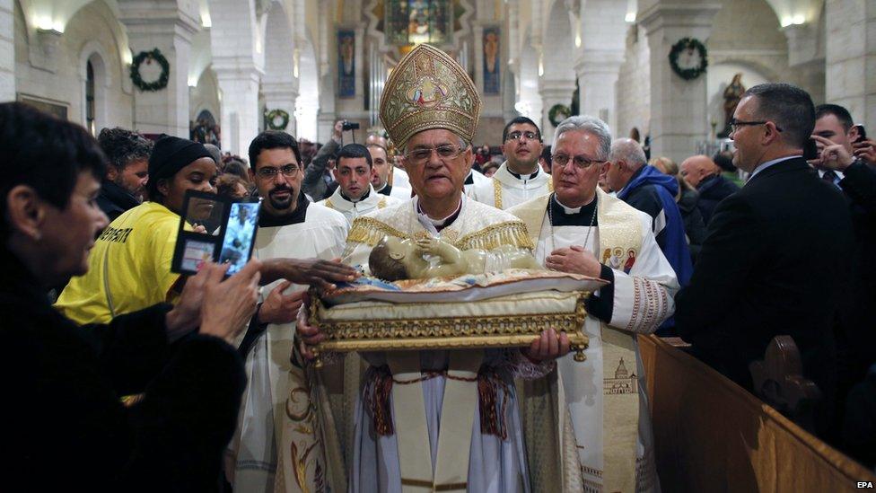 The Latin Patriarch of Jerusalem Fouad Twal carries a statuette of baby Jesus during a Christmas Midnight Mass at the Church of the Nativity in Bethlehem, the West Bank, 25 December 2014