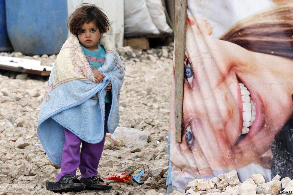 A Syrian refugee girl covers herself with a blanket as she stands outside tents at a makeshift settlement in Bar Elias in the Bekaa valley, 5 January 2015.