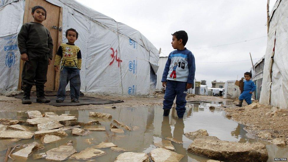 A Syrian refugee boy stands in a pool of water as he looks at others outside tents at a makeshift settlement in Bar Elias in the Bekaa valley, 5 January 2015