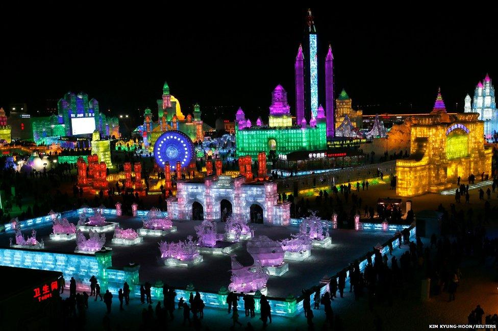 People visit ice sculptures illuminated by coloured lights