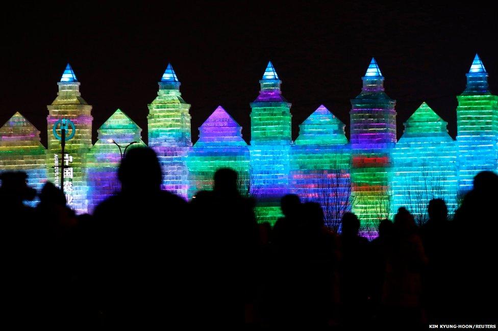 People heading to the 31st Harbin International Ice and Snow Festival venue are silhouetted against ice sculptures