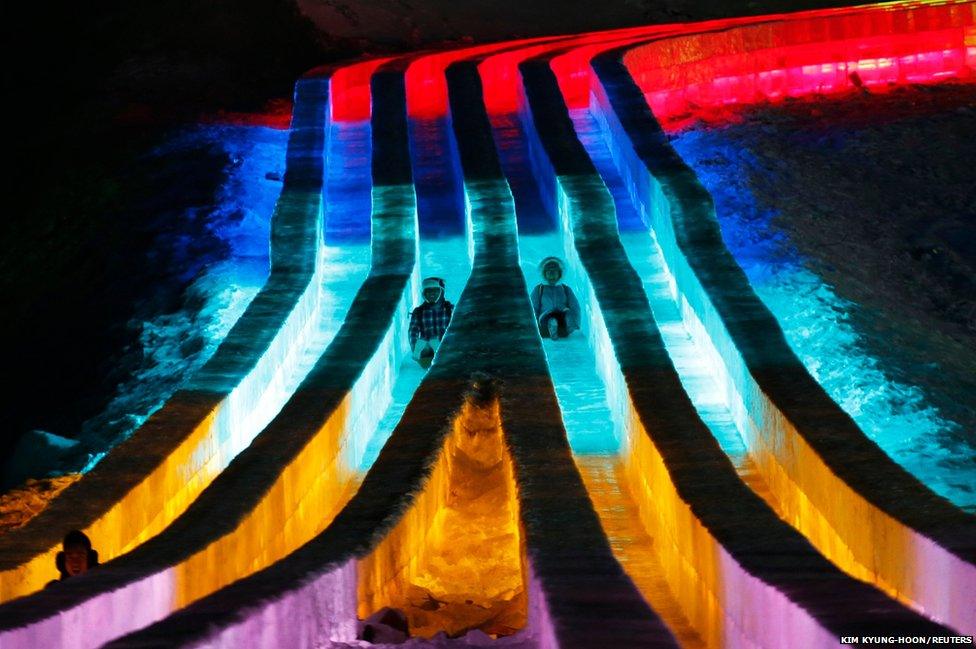 People ride slides on ice sculptures illuminated by coloured lights