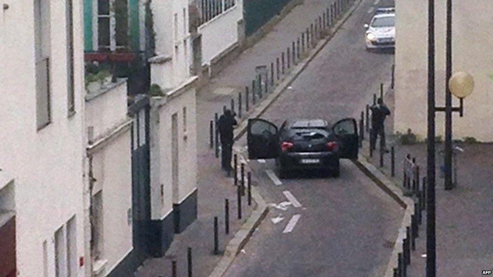 Armed gunmen face police officers near the offices of the French satirical newspaper Charlie Hebdo in Paris on 7 January 2015