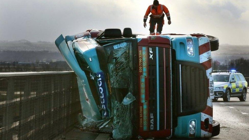 A man climbs on a lorry on its side after being blown over in strong winds on the Clackmannanshire Bridge over the Firth of Forth, Scotland