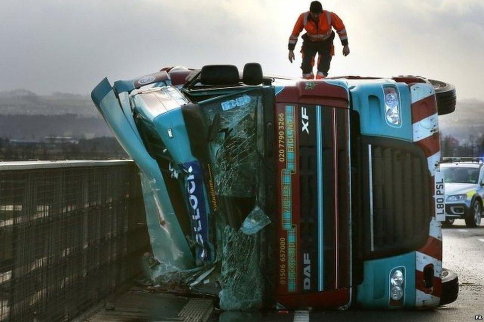 A man climbs on a lorry on its side after being blown over in strong winds on the Clackmannanshire Bridge over the Firth of Forth, Scotland