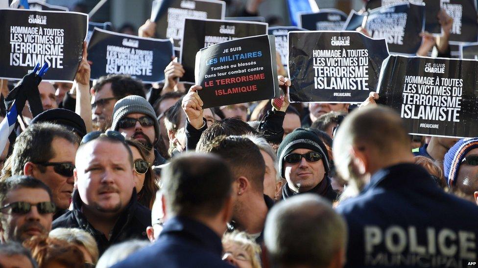 Policemen look on as people hold signs reading "Tribute to all the victims of Islamist terrorism" during a Unity rally Marche Republicaine in Beaucaire, southern France