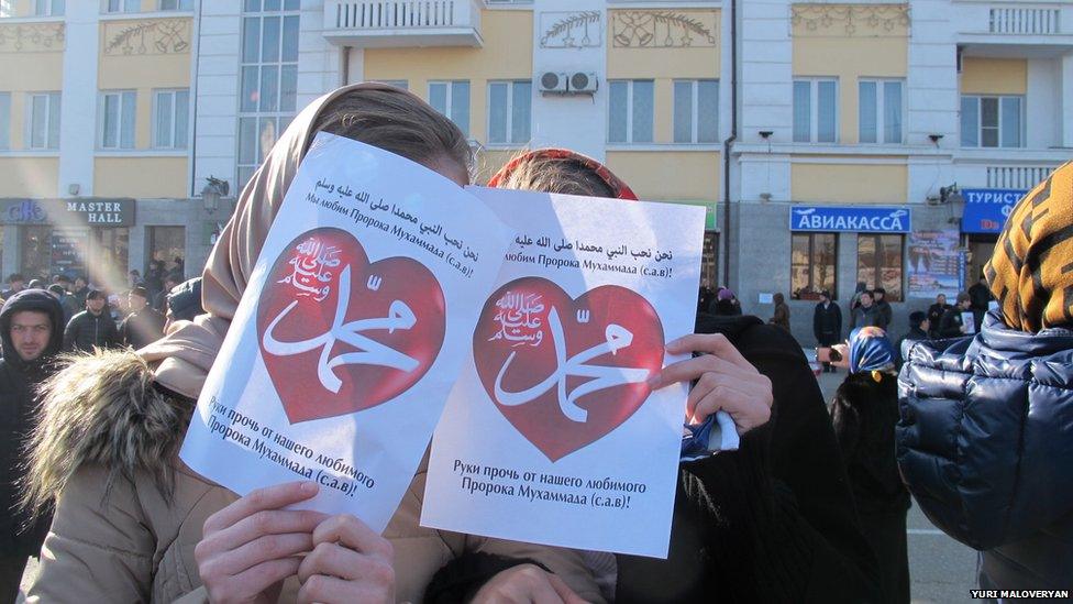 Protesters holding placards with signs translated to 'hands off from our beloved Prophet Muhammad'