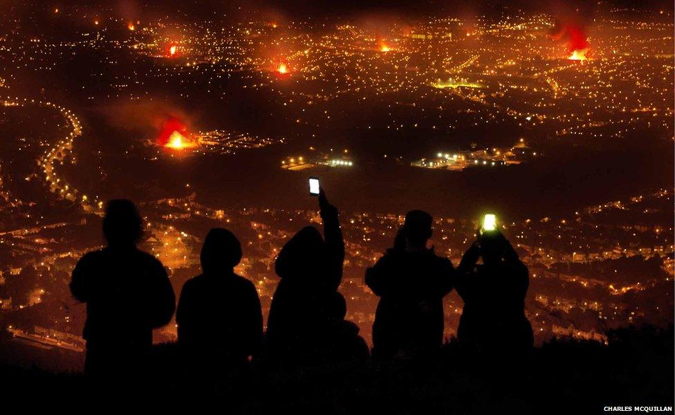 Young people taking photos of Eleventh Night bonfires from Cave Hill, overlooking Belfast