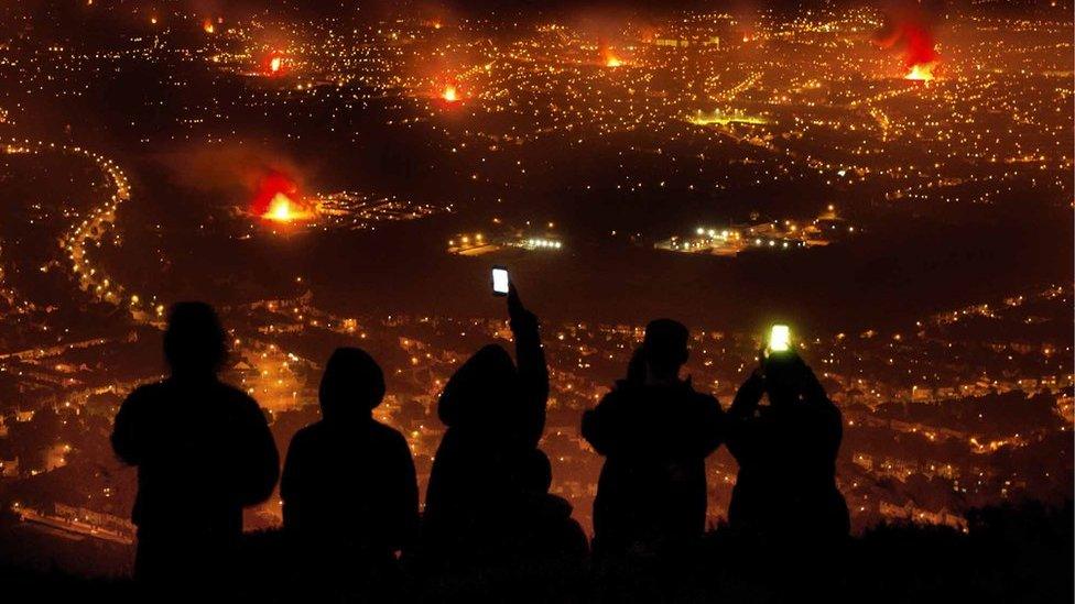 Young people taking photos of Eleventh Night bonfires from Cave Hill, overlooking Belfast