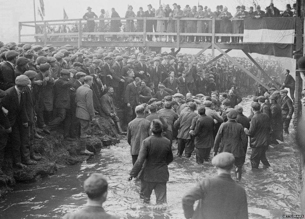 February 1928: Crowds watch the annual Shrovetide football game, which is 'kicked - off' in the stream which runs through the Derbyshire town of Ashbourne